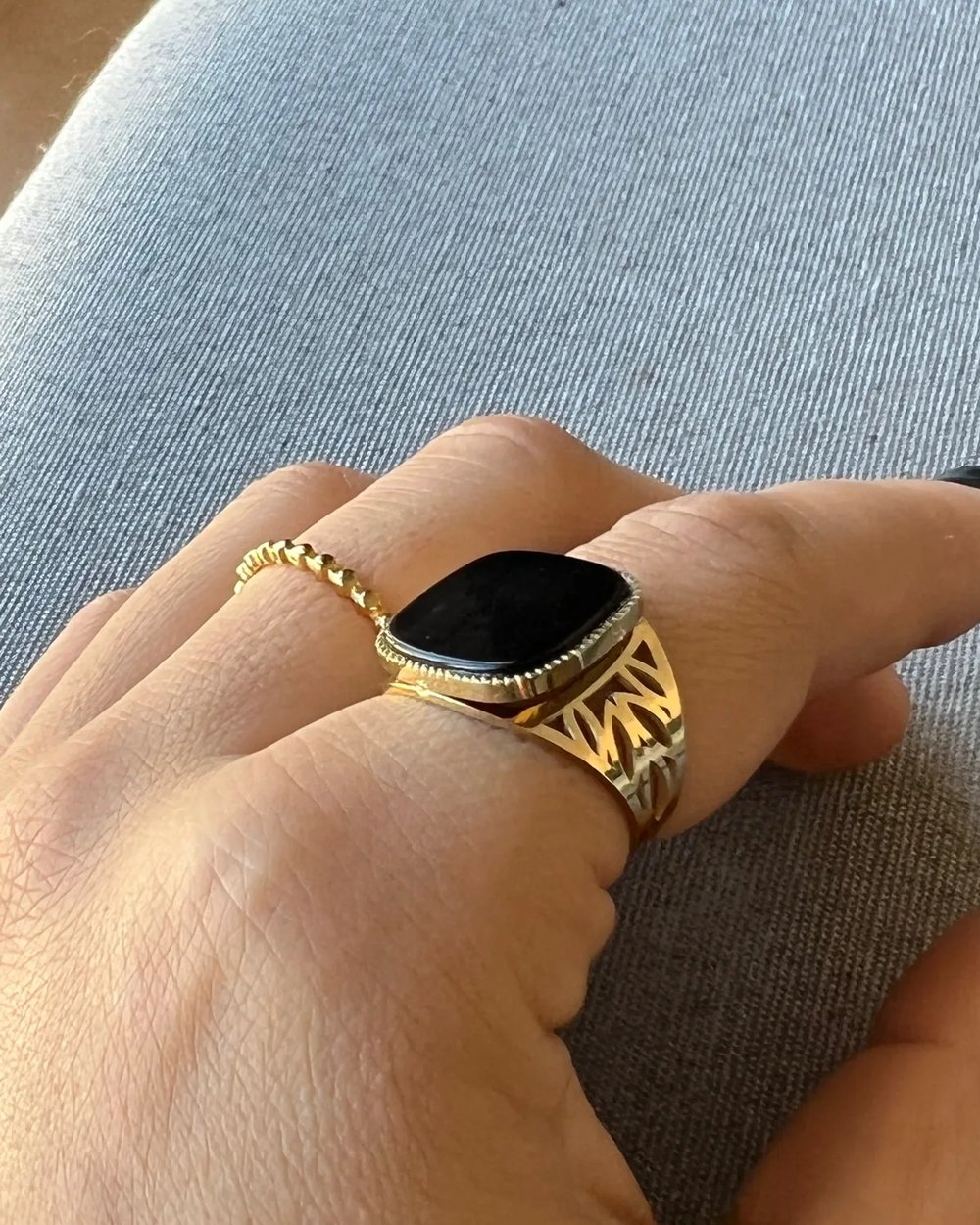 Bague chevalière dorée à pierre noire portée à la main